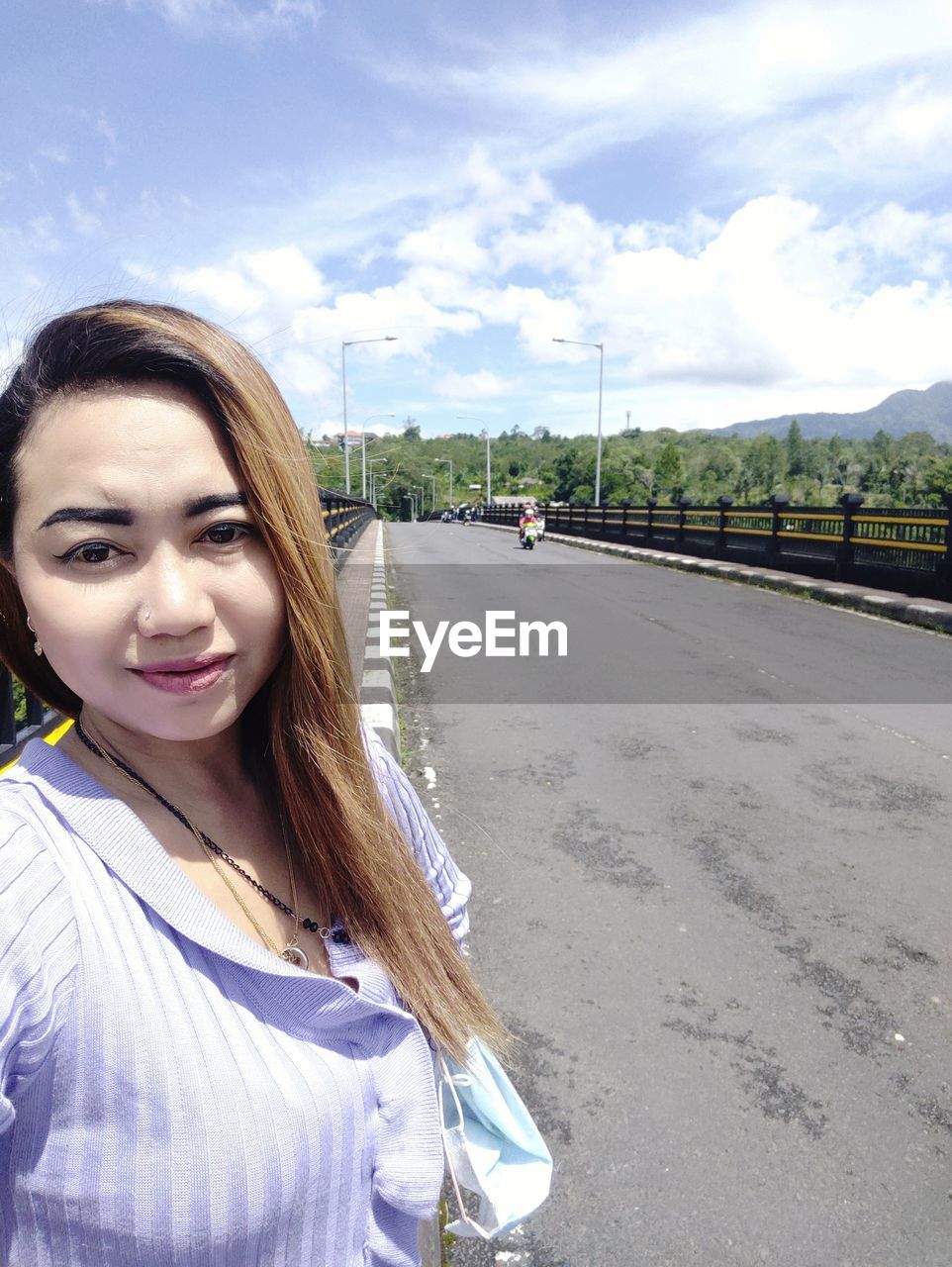 PORTRAIT OF SMILING YOUNG WOMAN STANDING ON ROAD