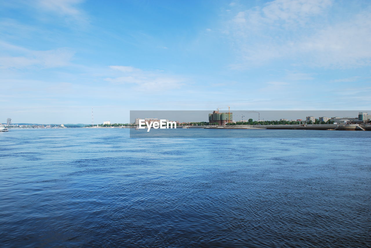 CITY AT WATERFRONT AGAINST CLOUDY SKY