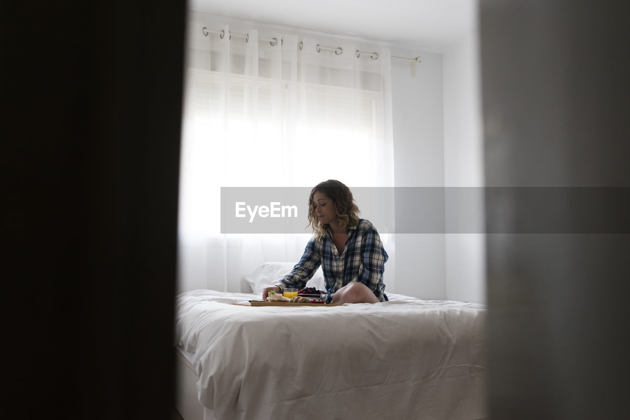 View thru a door ajar of woman having breakfast on bed.