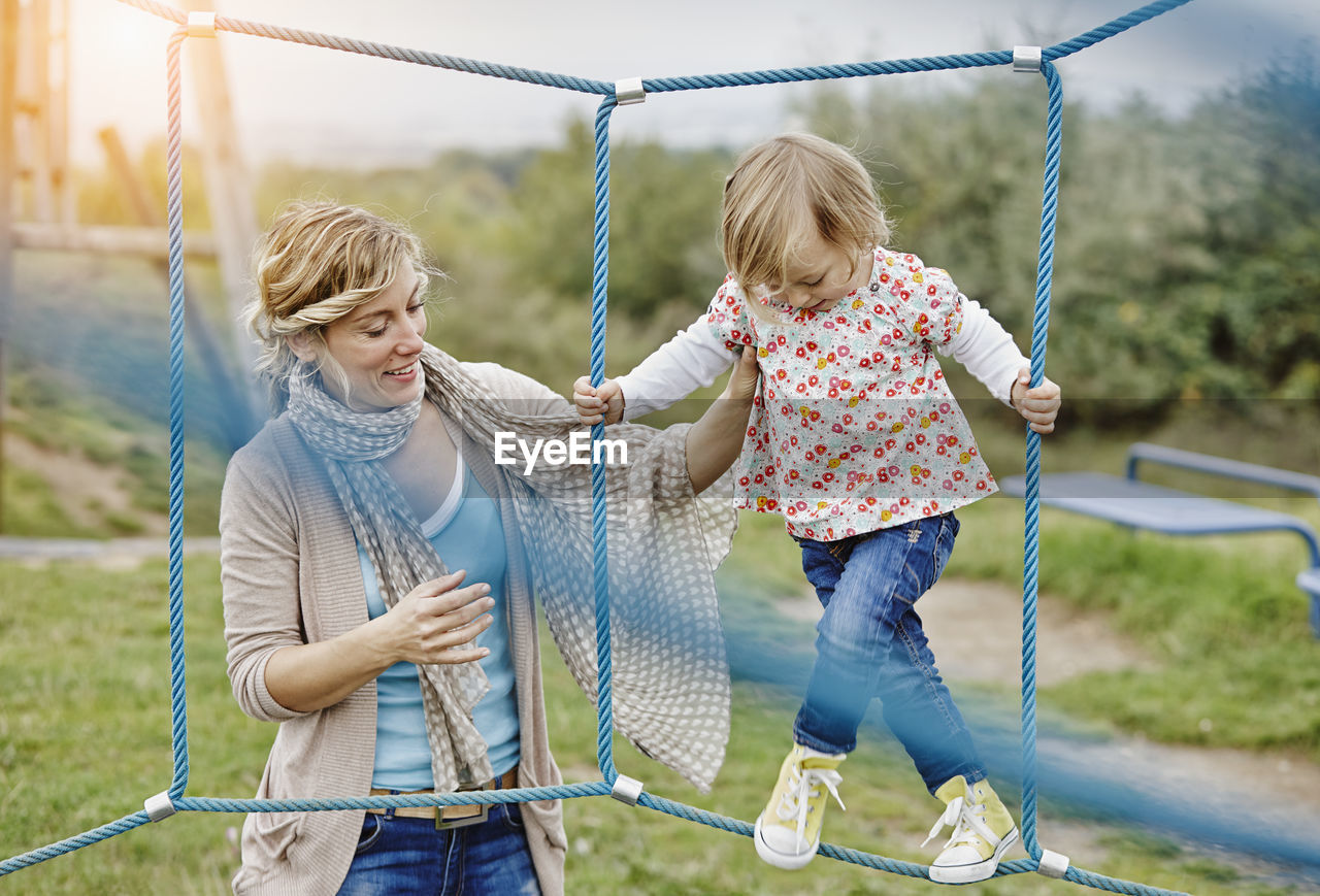 Girl on playground in climbing net supported by mother