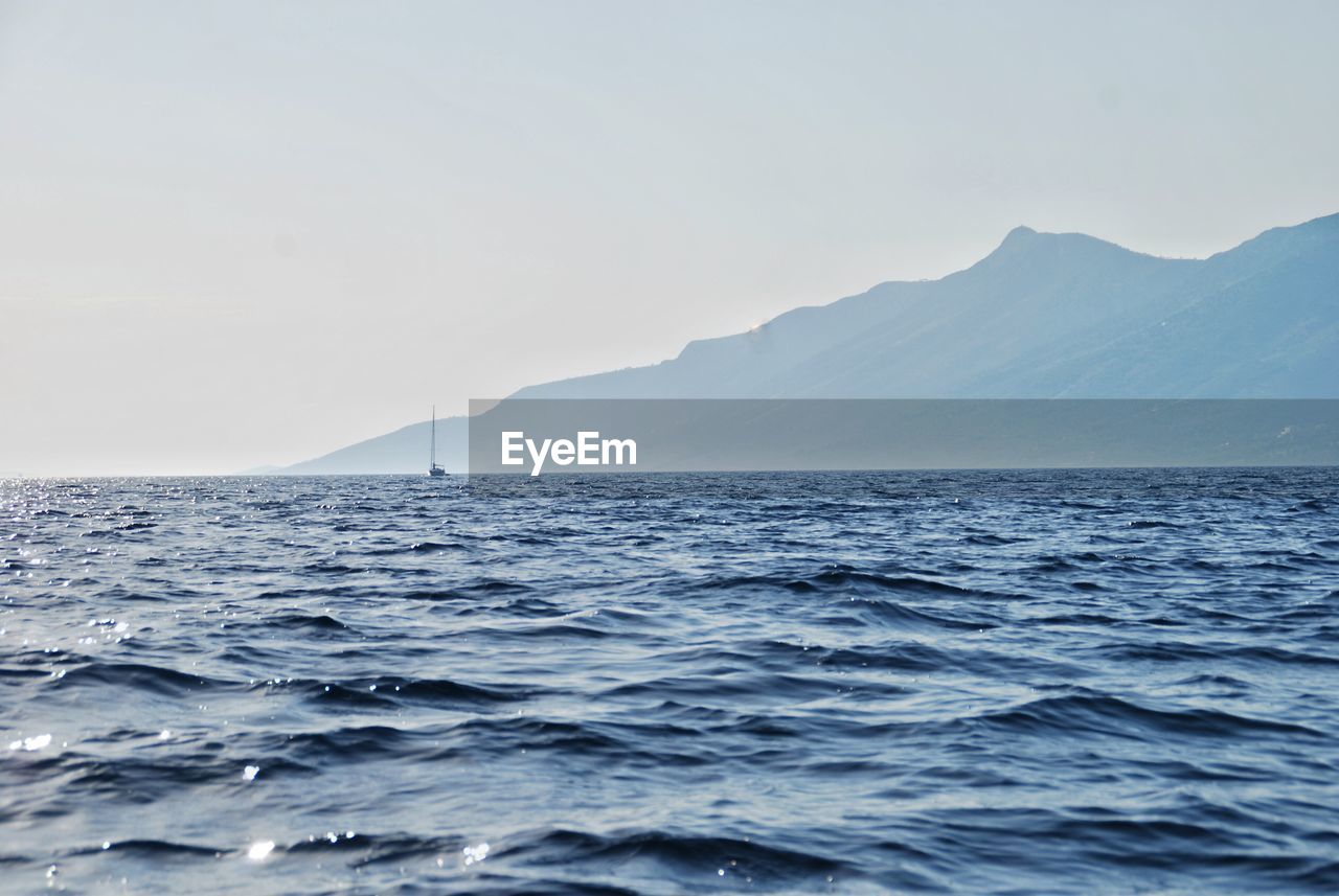 Scenic view of sea by mountain against clear sky