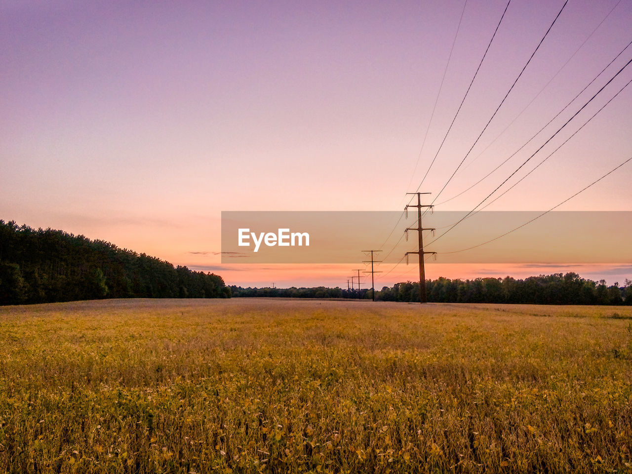 Power lines on field against sky during sunset