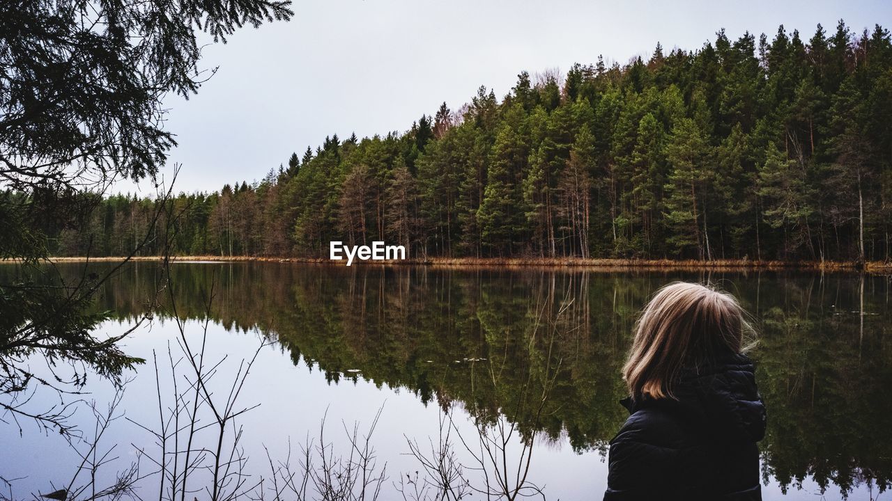 Rear view of woman standing against lake in forest