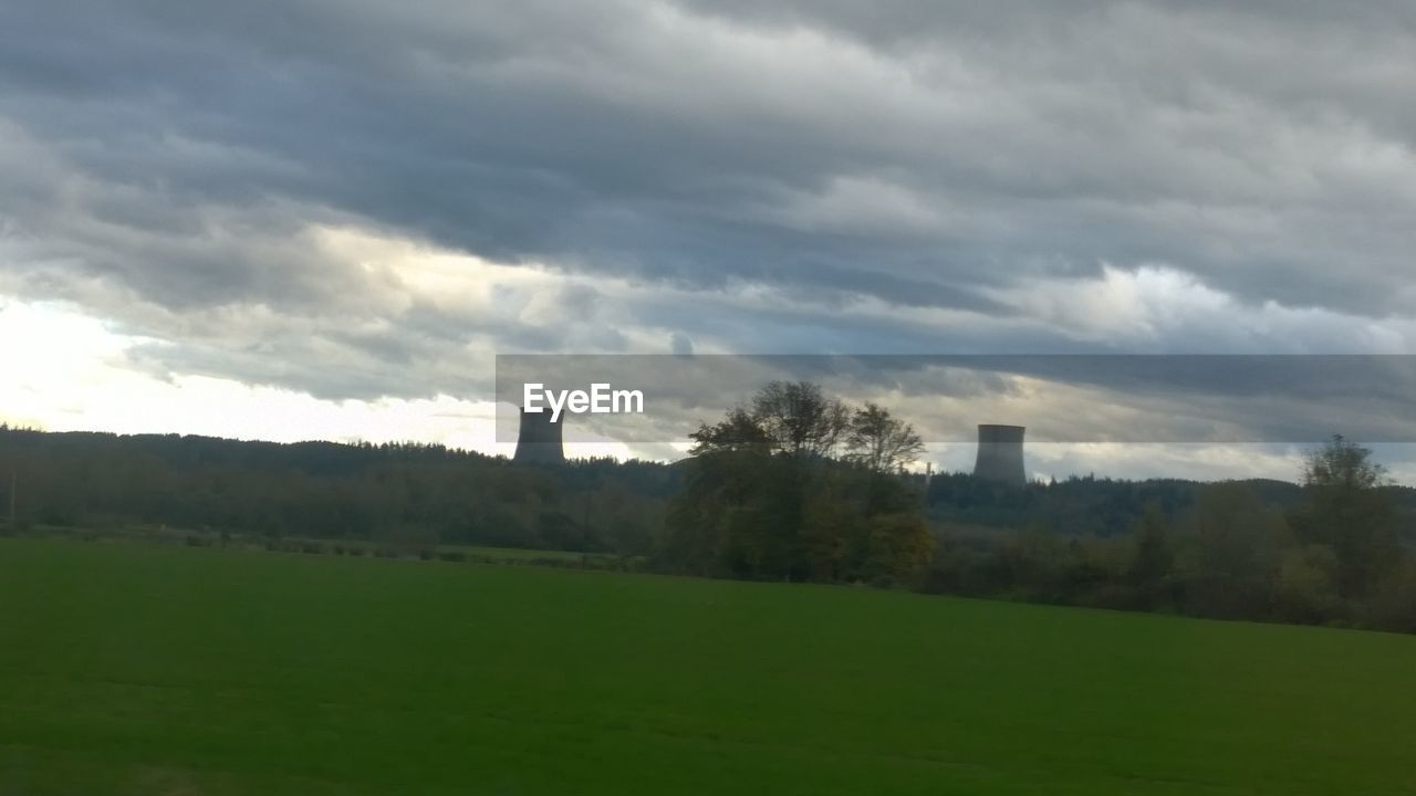 TREES ON GRASSY FIELD AGAINST CLOUDY SKY