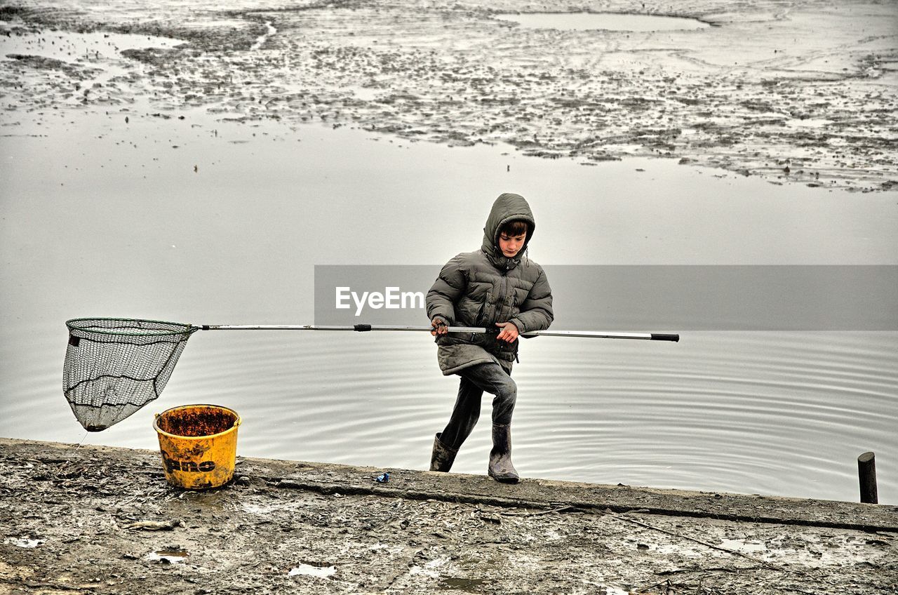 Boy carrying fishing net while standing in lake