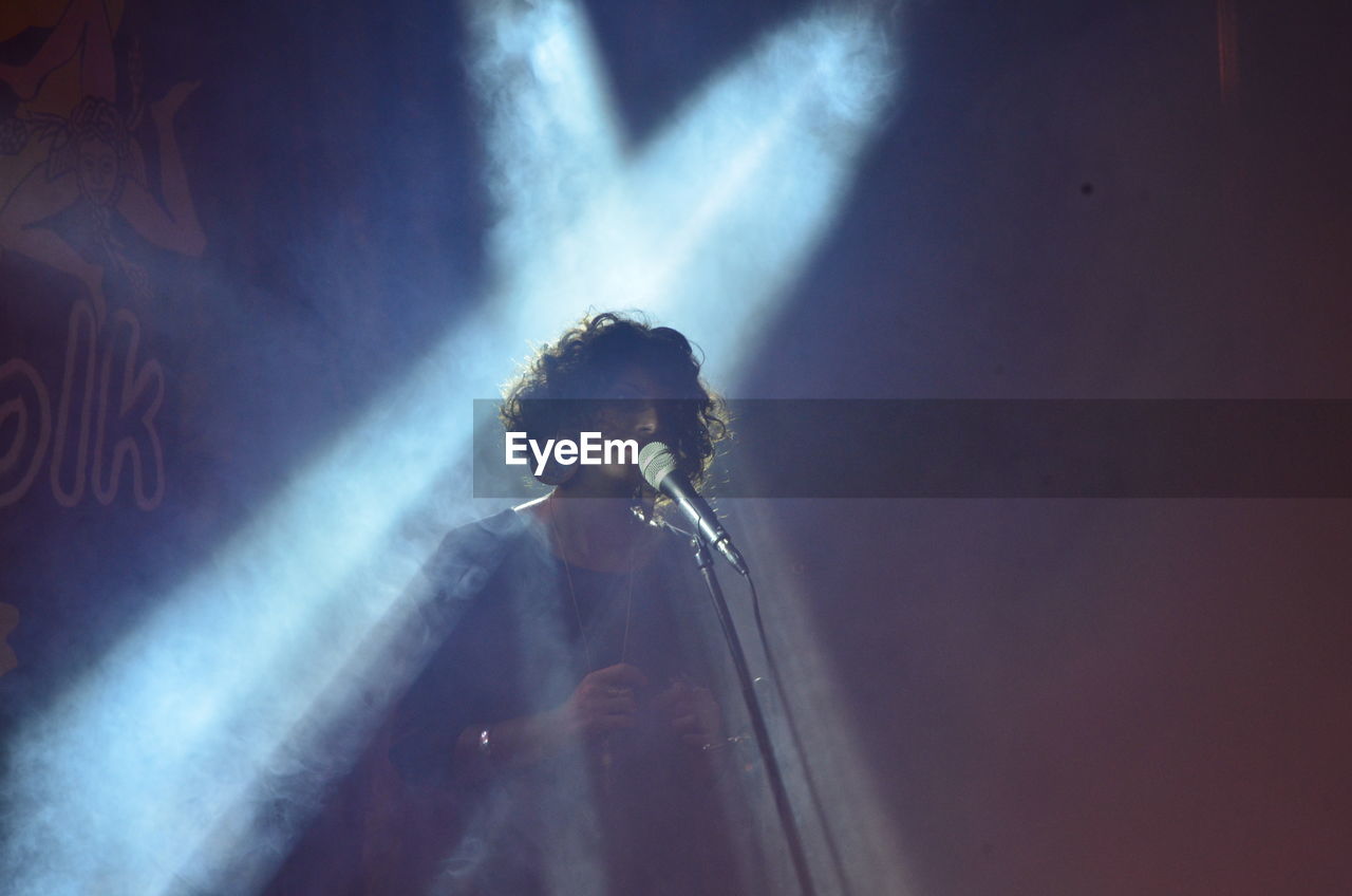 FULL LENGTH OF YOUNG MAN STANDING AGAINST ILLUMINATED WALL AT MUSIC CONCERT