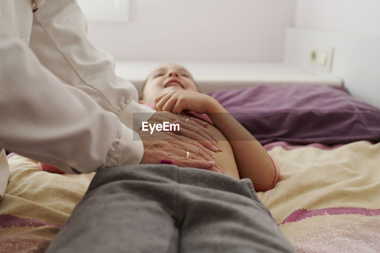 Female doctor examining a little girl's abdomen in her room. home doctor concept