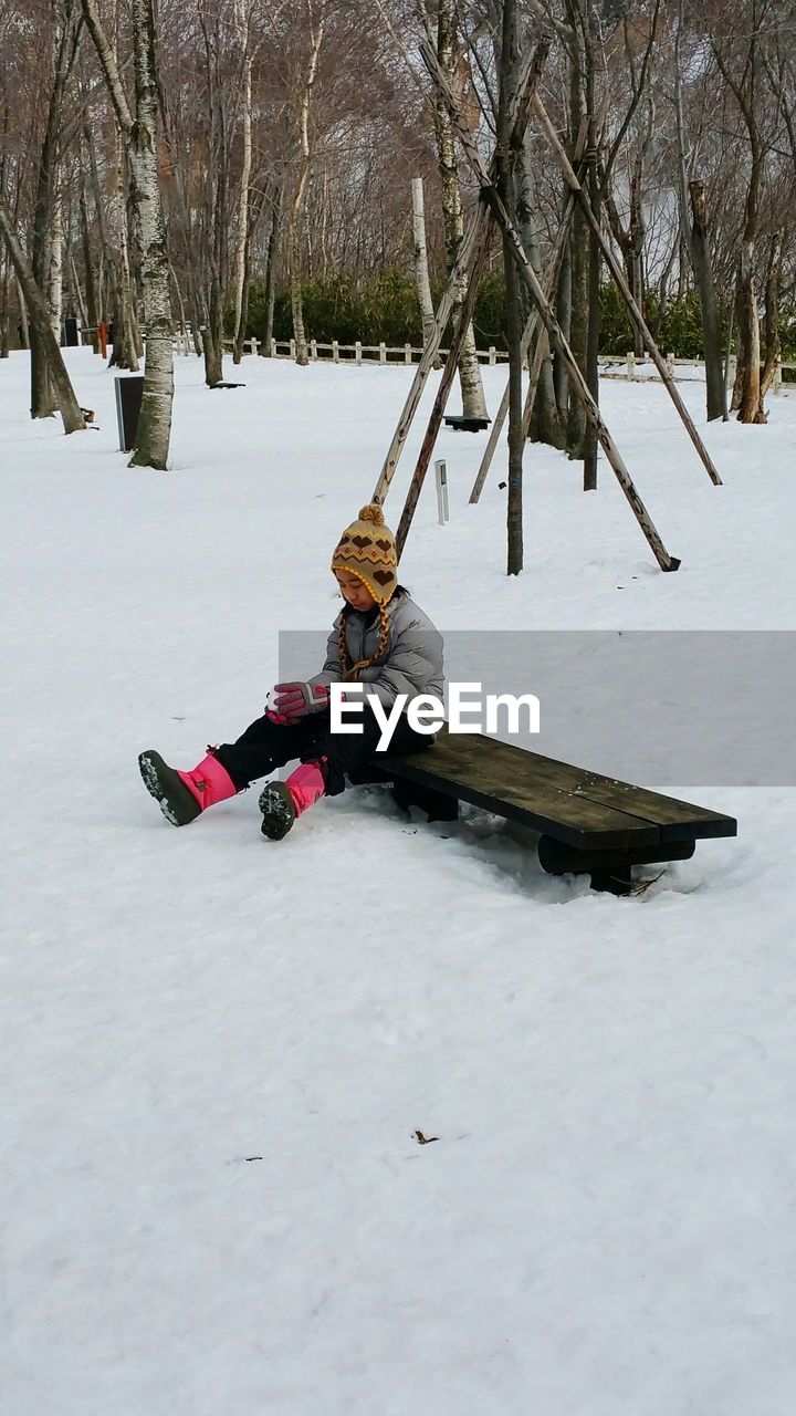 Full length of girl sitting on bench over snow