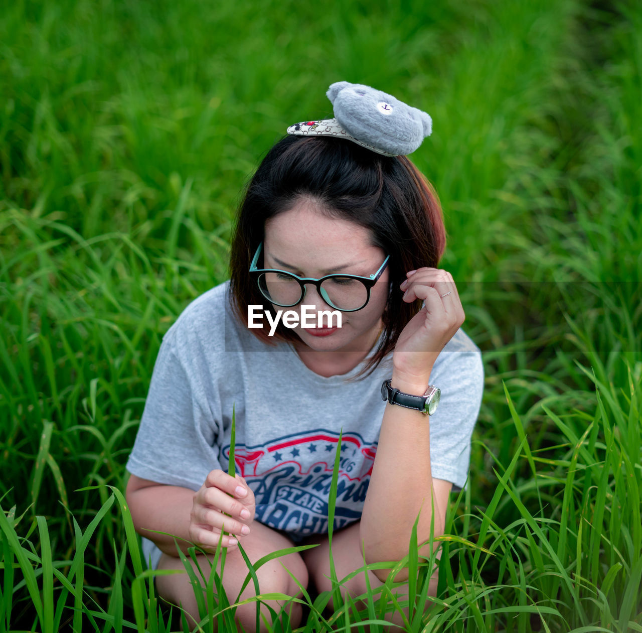 Woman wearing eyeglasses crouching on field against sky