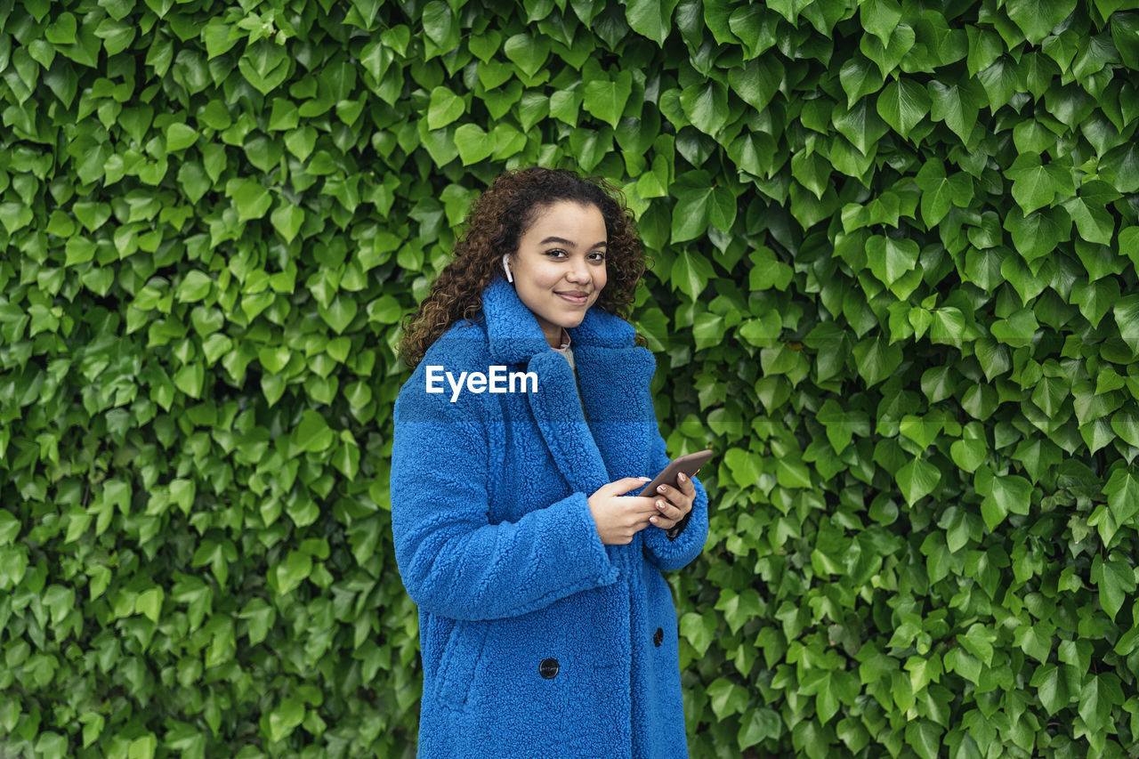 Young woman using phone while standing on green plant