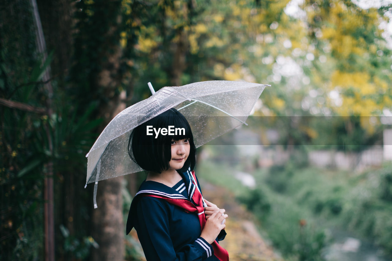 Woman holding umbrella standing in rain during rainy season