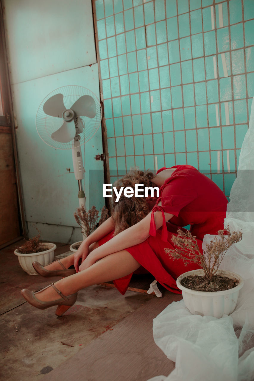 Young woman in red dress sitting amidst potted plants at home