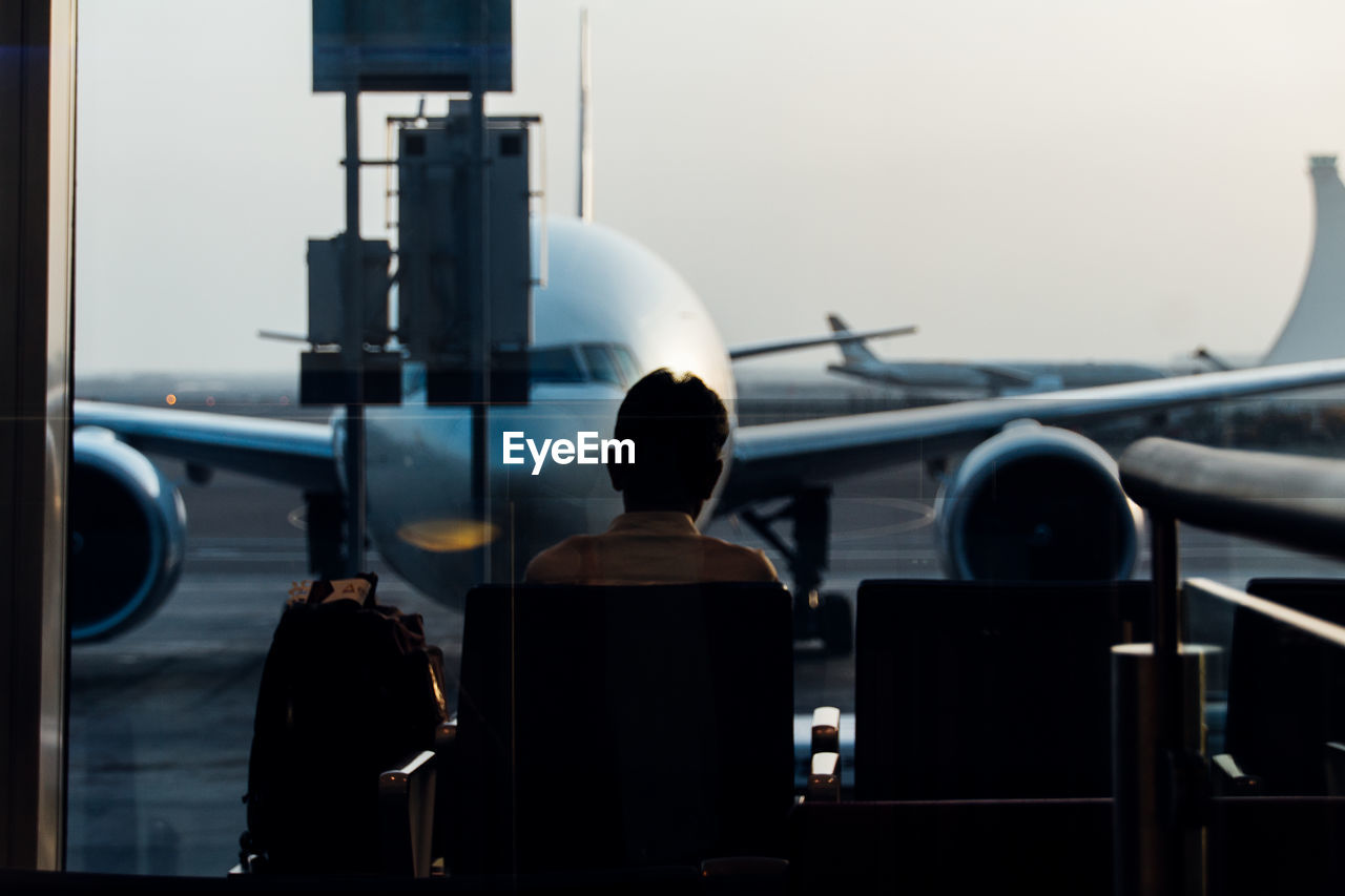 Rear view of man looking at airplane while sitting in airport