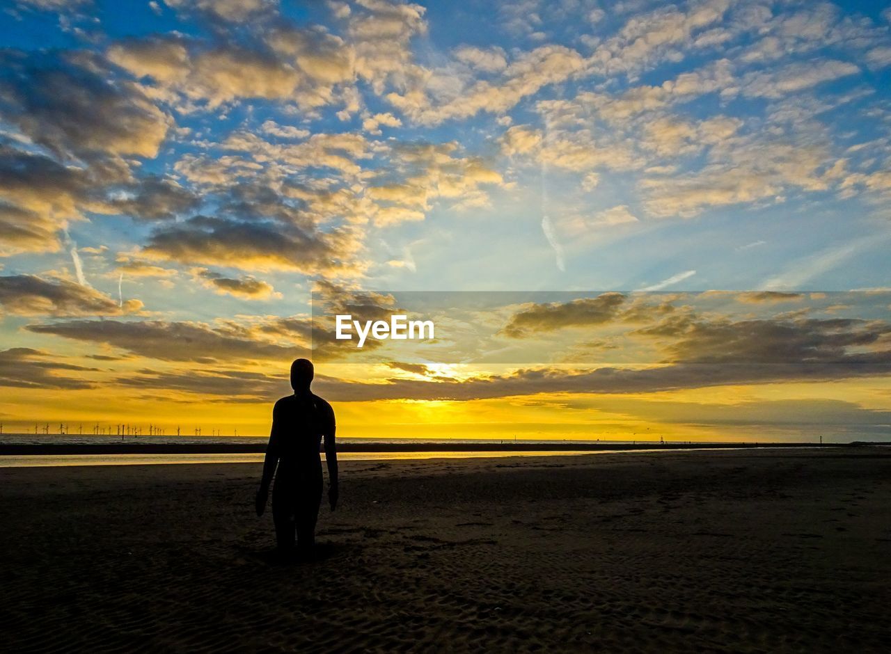 SILHOUETTE MAN STANDING AT BEACH DURING SUNSET