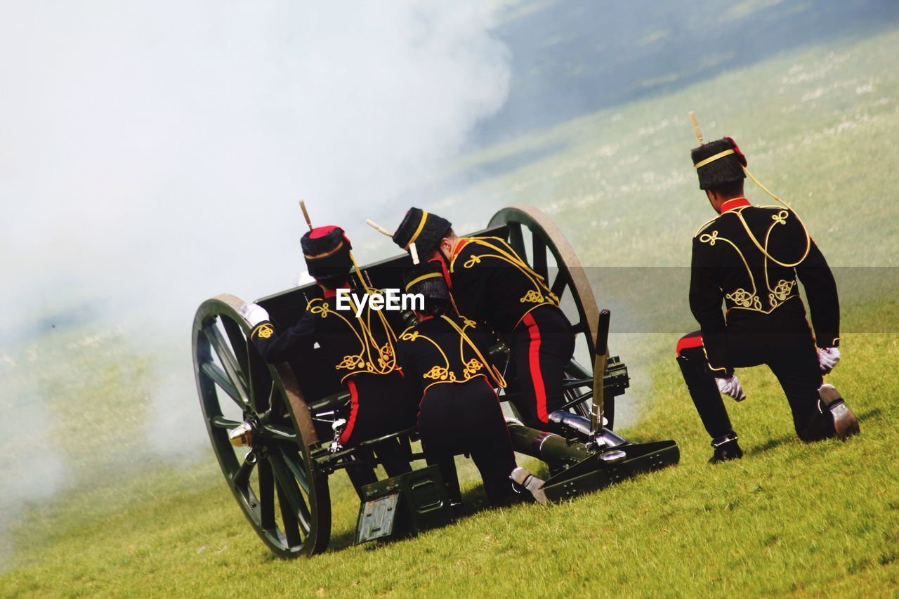 Rear view of army soldiers with metallic wheels on grassy field