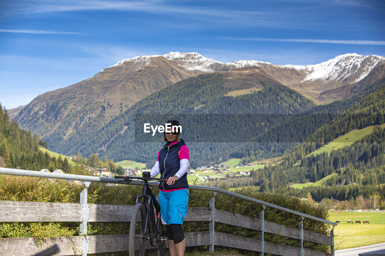 Portrait of woman standing with bicycle by railing against mountains
