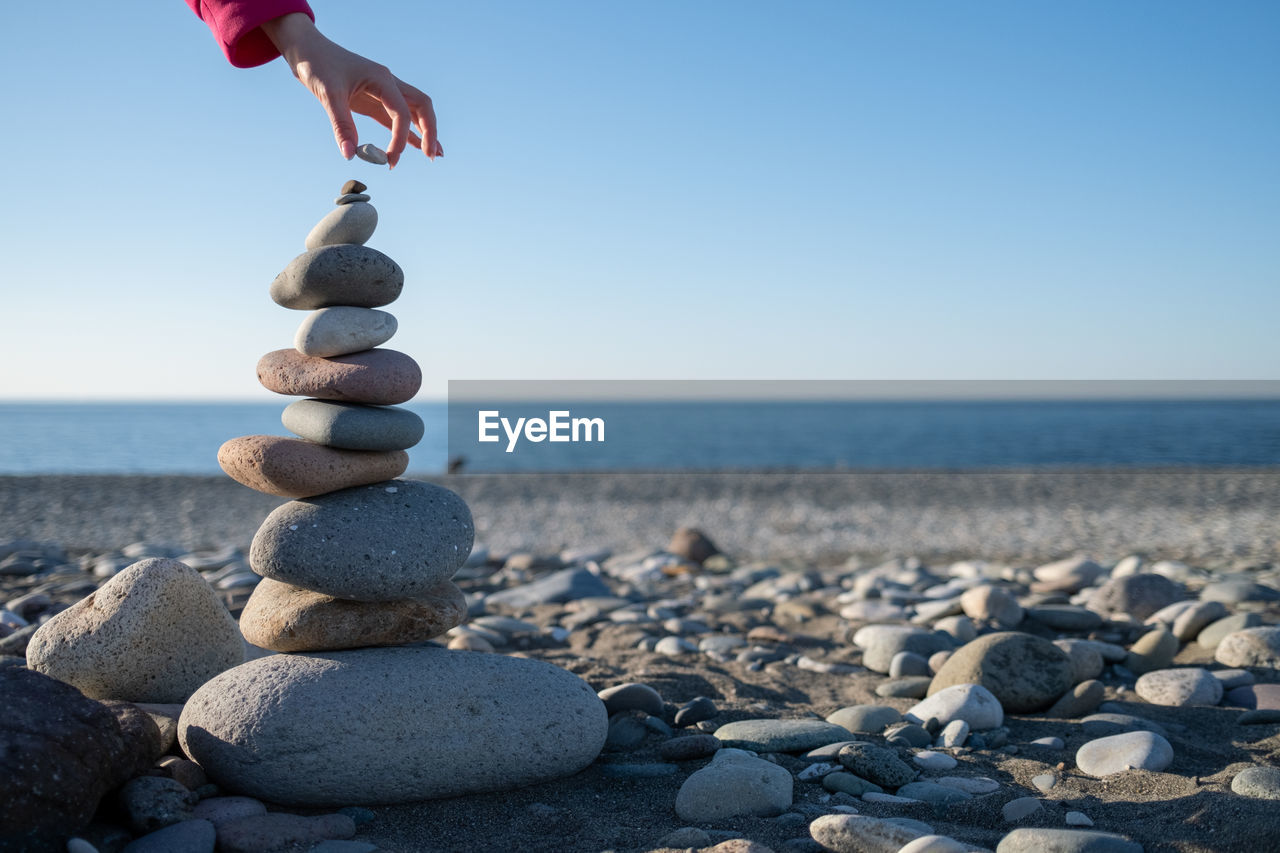 Hand puts a stone on tower on beach. house by sea. background for real estate advertising. 