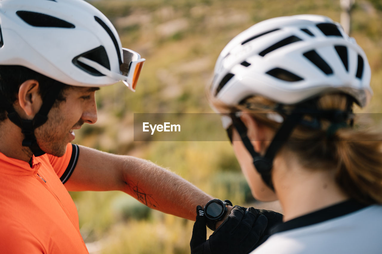 High angle of bicyclists in helmets standing together on hill and checking time on wristwatch during training