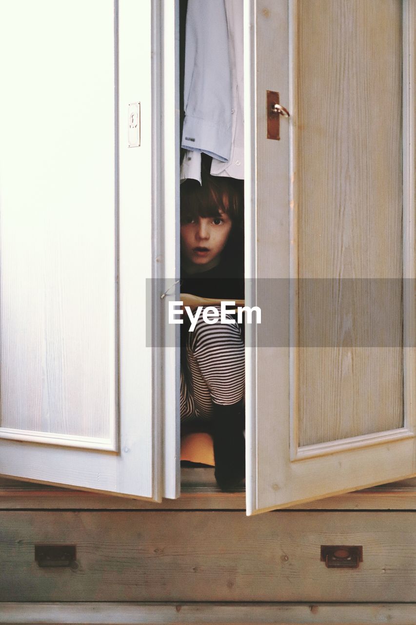 Portrait of cute boy hiding in closet at home