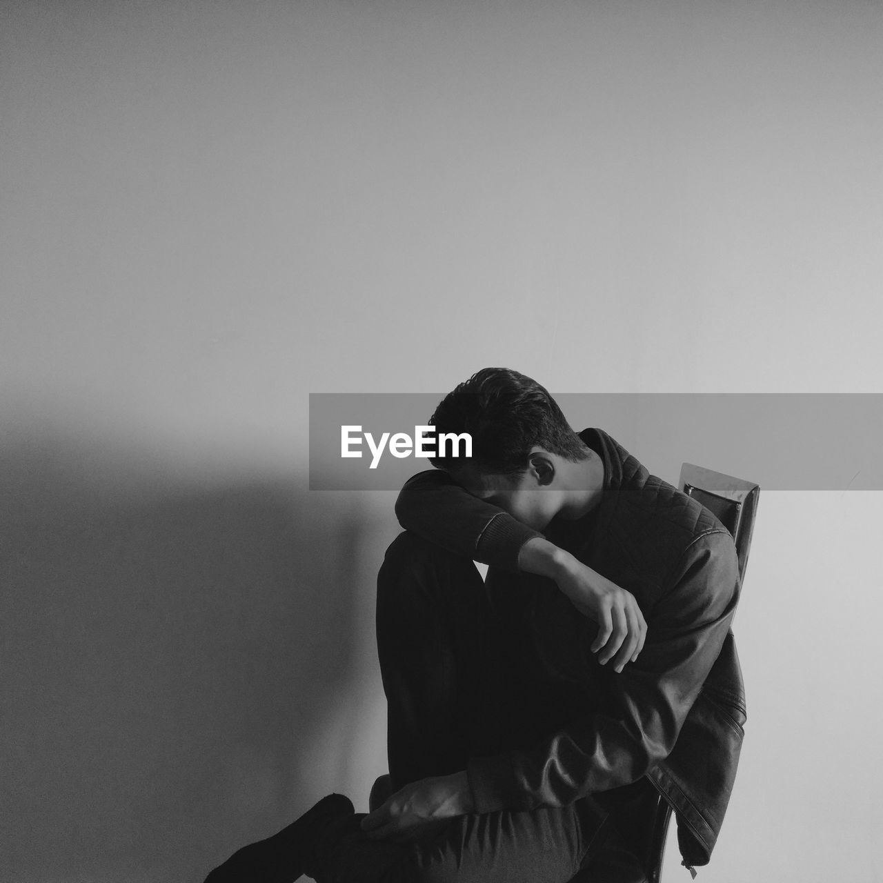 Depressed young man sitting against wall