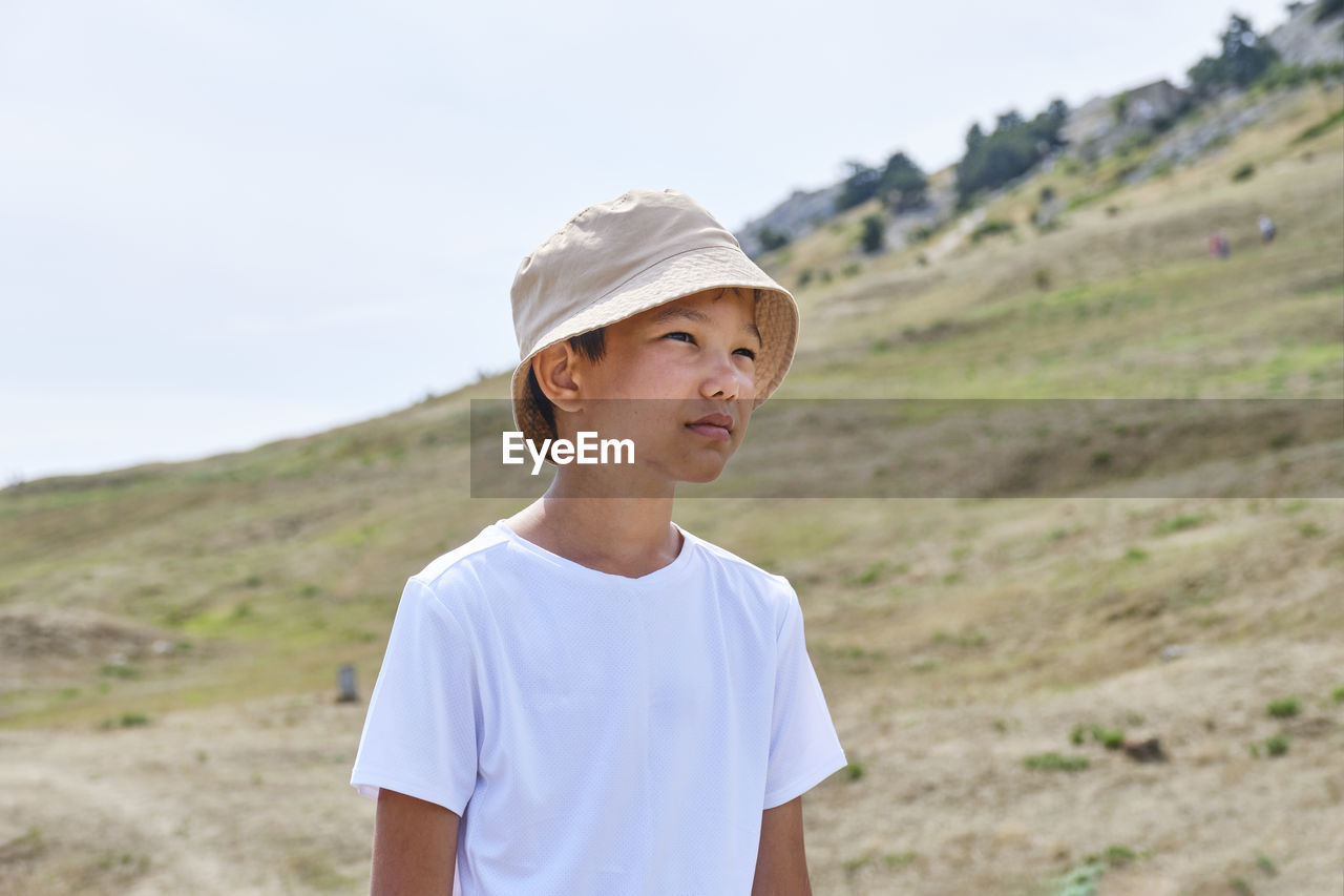 Half-length portrait of an asian boy in a white t-shirt and a panama hat on a background of nature.