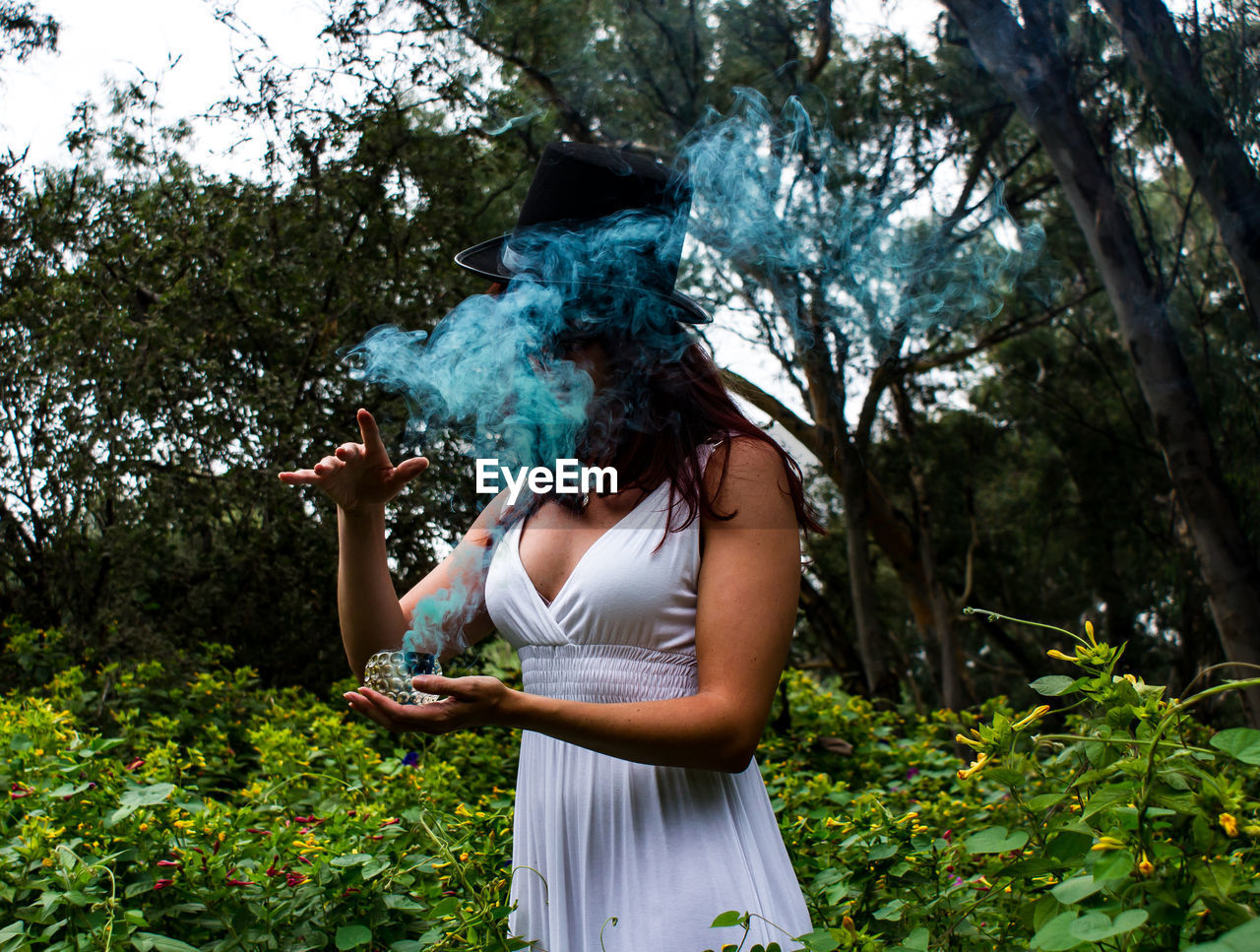 Woman stirring up blue smoke in garden 