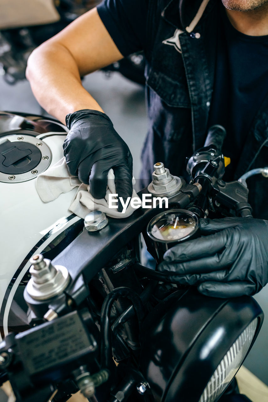 Midsection of mature mechanic cleaning motorcycle in garage