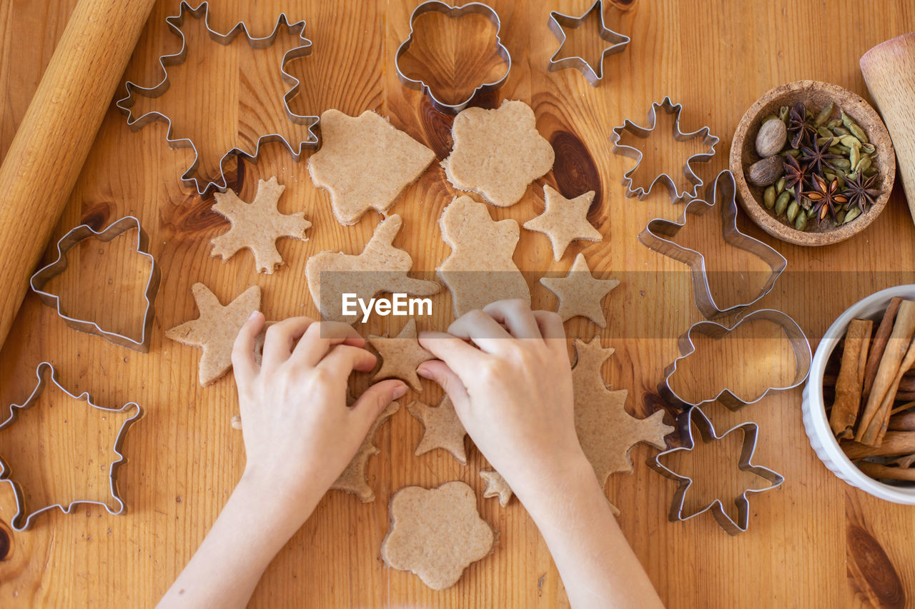 Children with their mother cut out christmas gingerbread cookies on the table from rolled dough. 