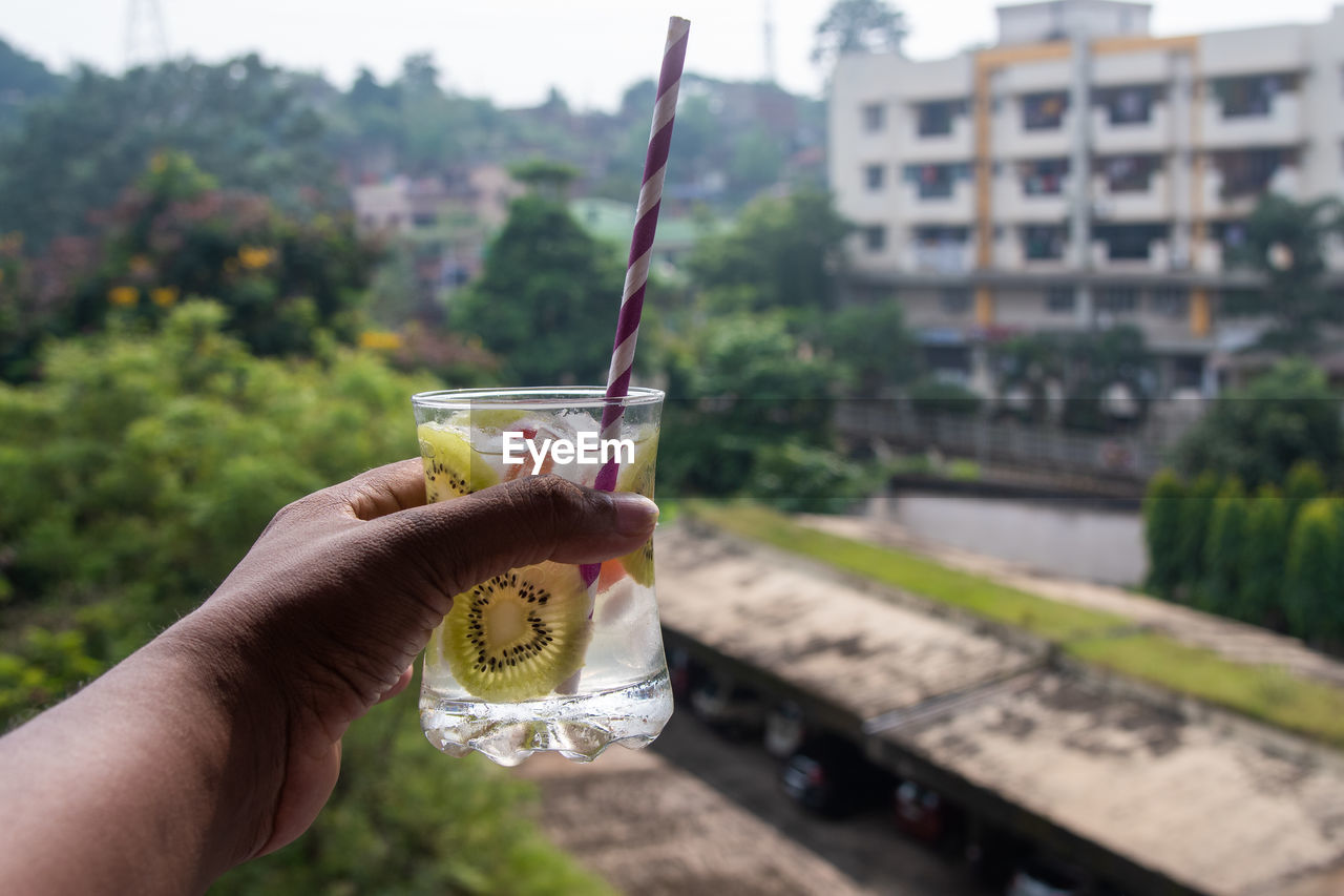 hand, food and drink, holding, drink, refreshment, one person, focus on foreground, food, soft drink, personal perspective, freshness, architecture, day, lifestyles, adult, glass, fruit, tree, sky, nature, drinking glass, outdoors, alcohol, healthy eating, city, household equipment, water, plant, drinking, drinking straw, leisure activity, built structure, close-up, alcoholic beverage