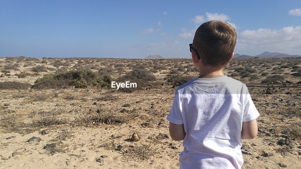 Rear view of boy standing at desert against sky during sunny day