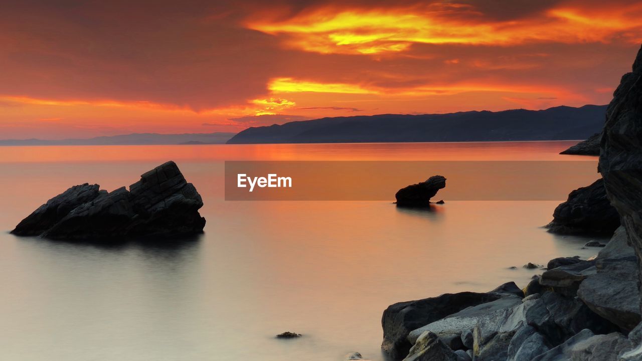 Rocks in sea against sky during sunset