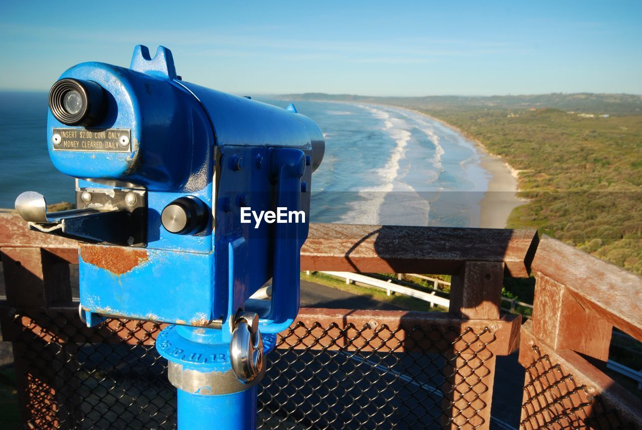 Close-up of coin-operated binoculars by sea against blue sky