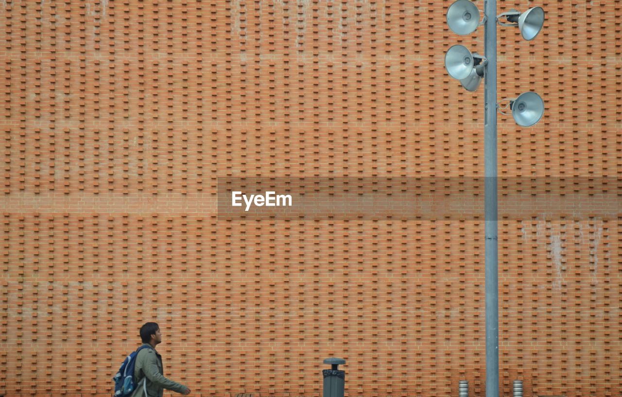 Man walking towards megaphones by brown wall