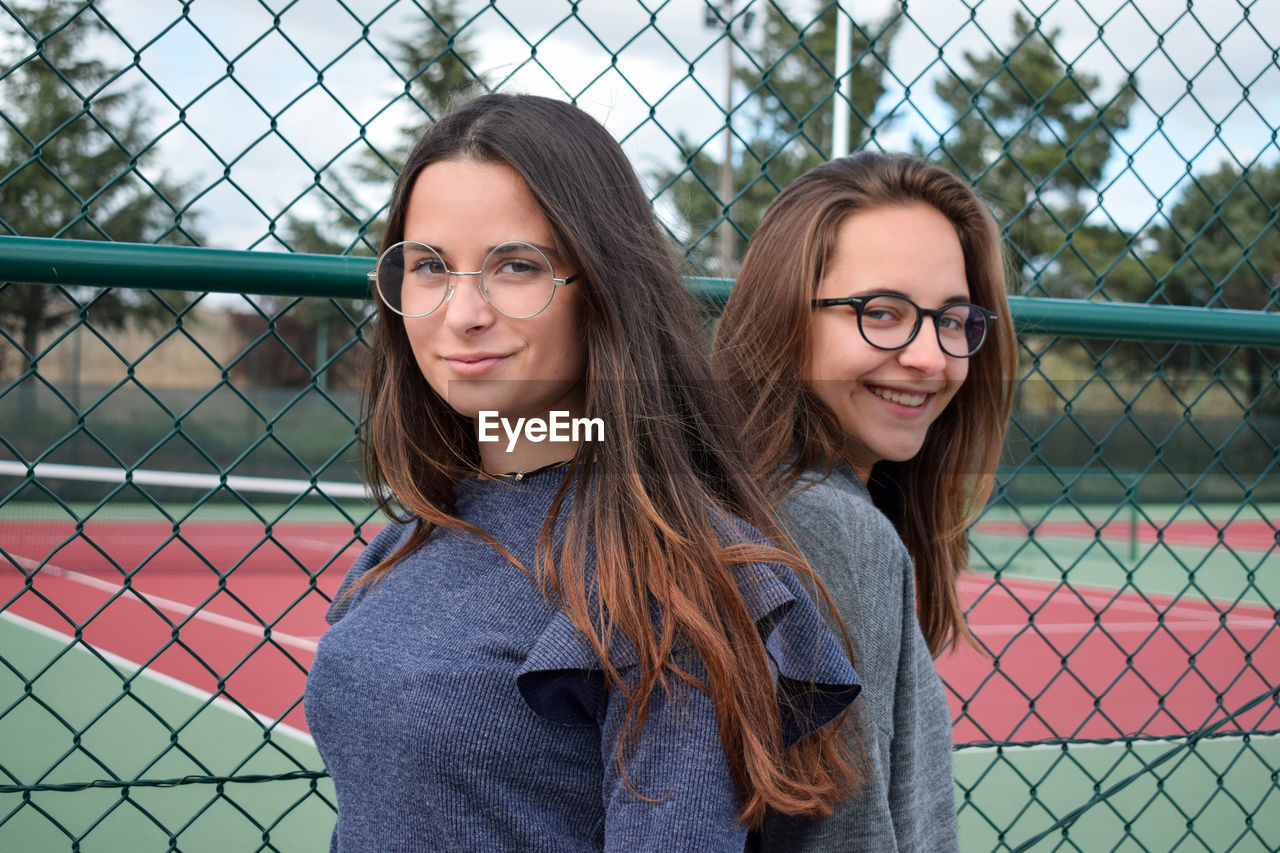 Portrait of smiling friends standing by fence