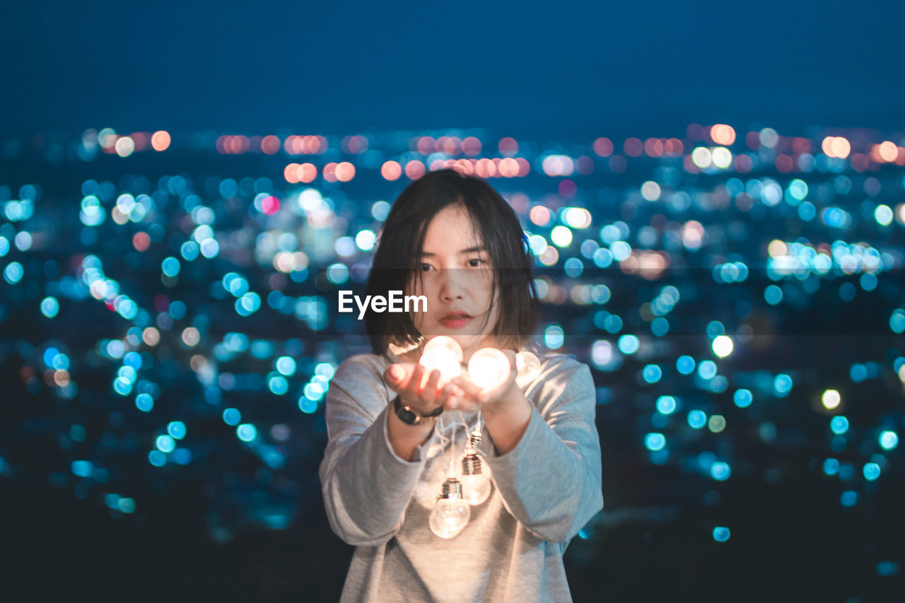 Portrait of young woman holding illuminated light at night