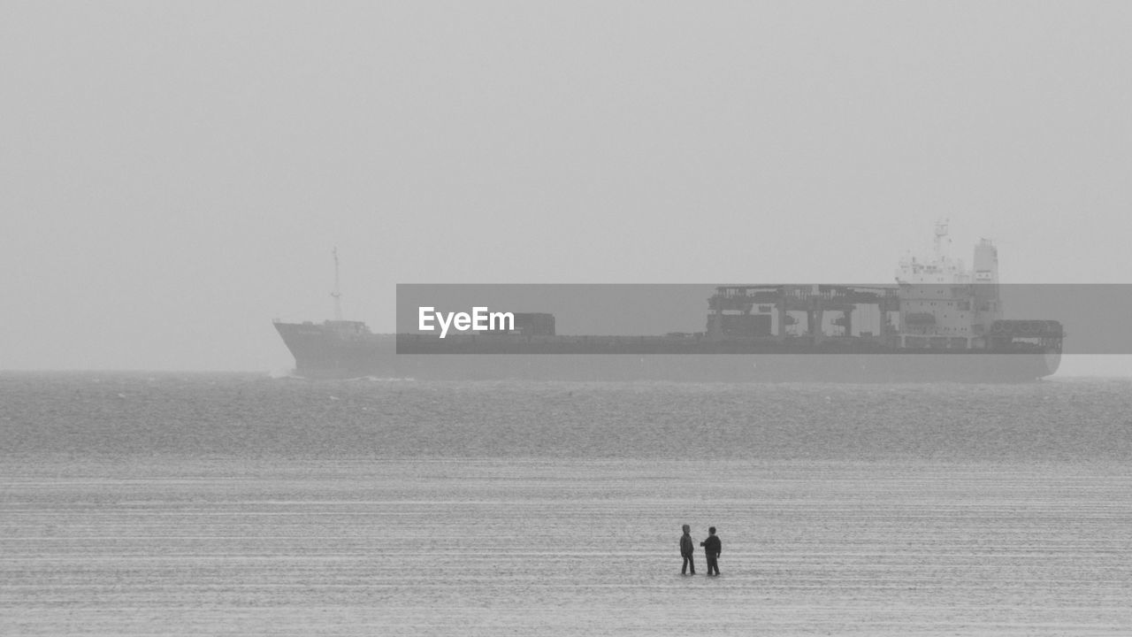 Two boys playing in the wadden sea with container ship in the background