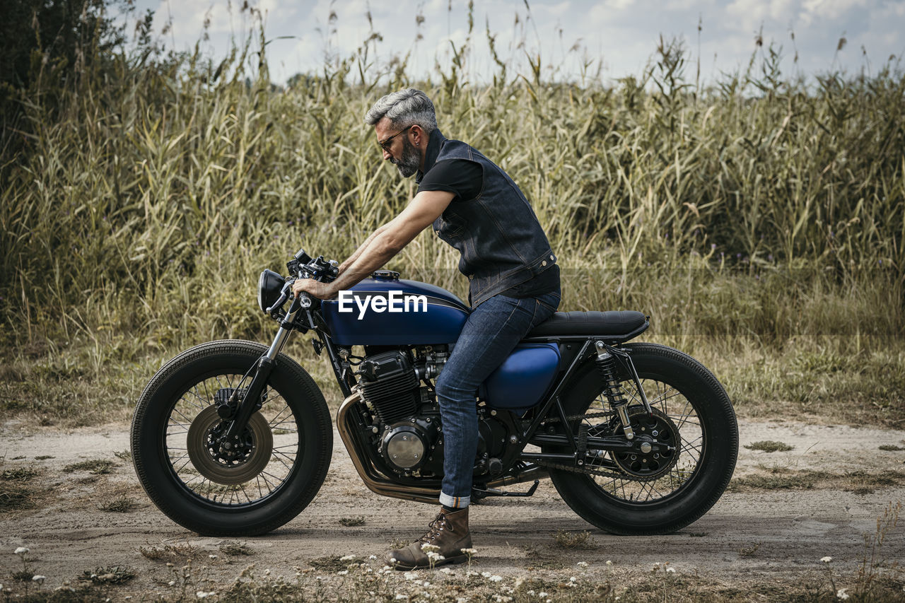 Mature man sitting on motorcycle by plants