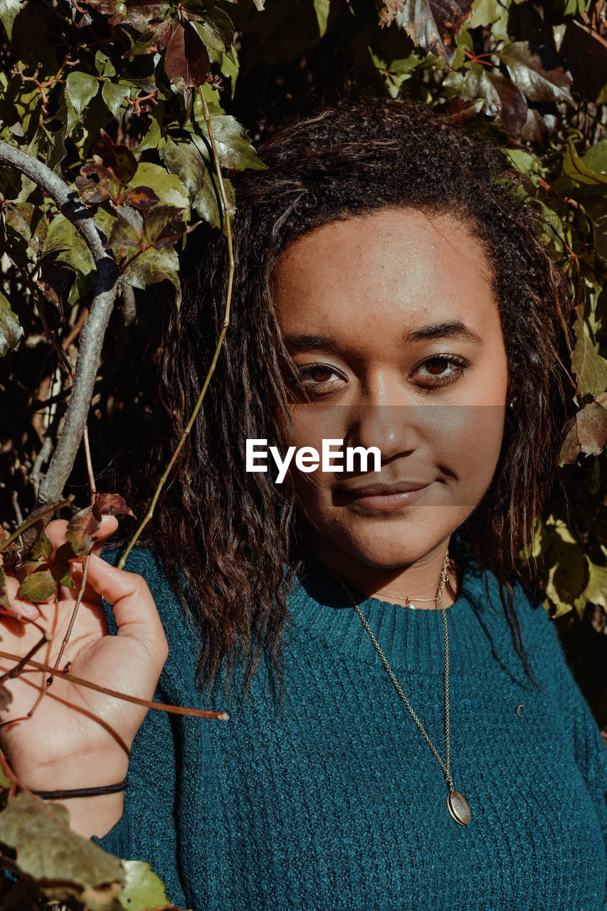 Portrait of beautiful young woman standing against plants