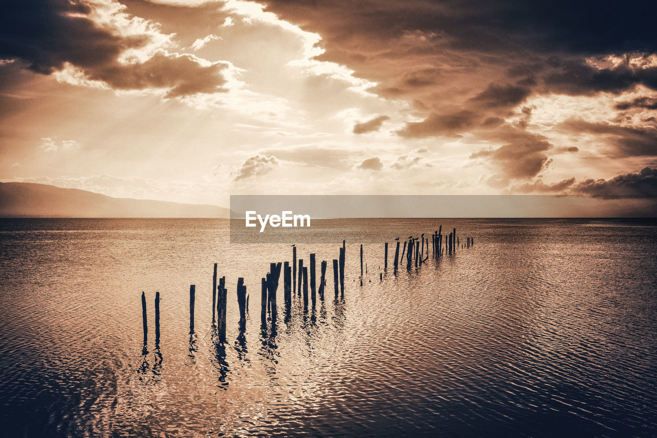 Wooden posts in sea against sky during sunset