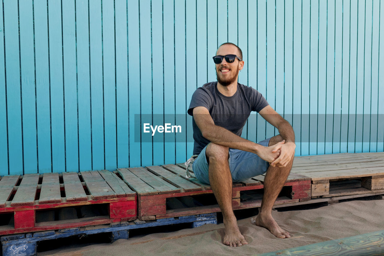 Portrait of young man sitting against blue wall