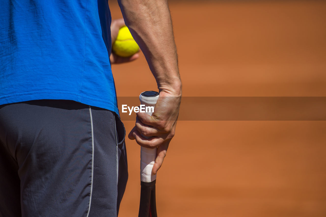 Midsection of player with ball and tennis racket on court