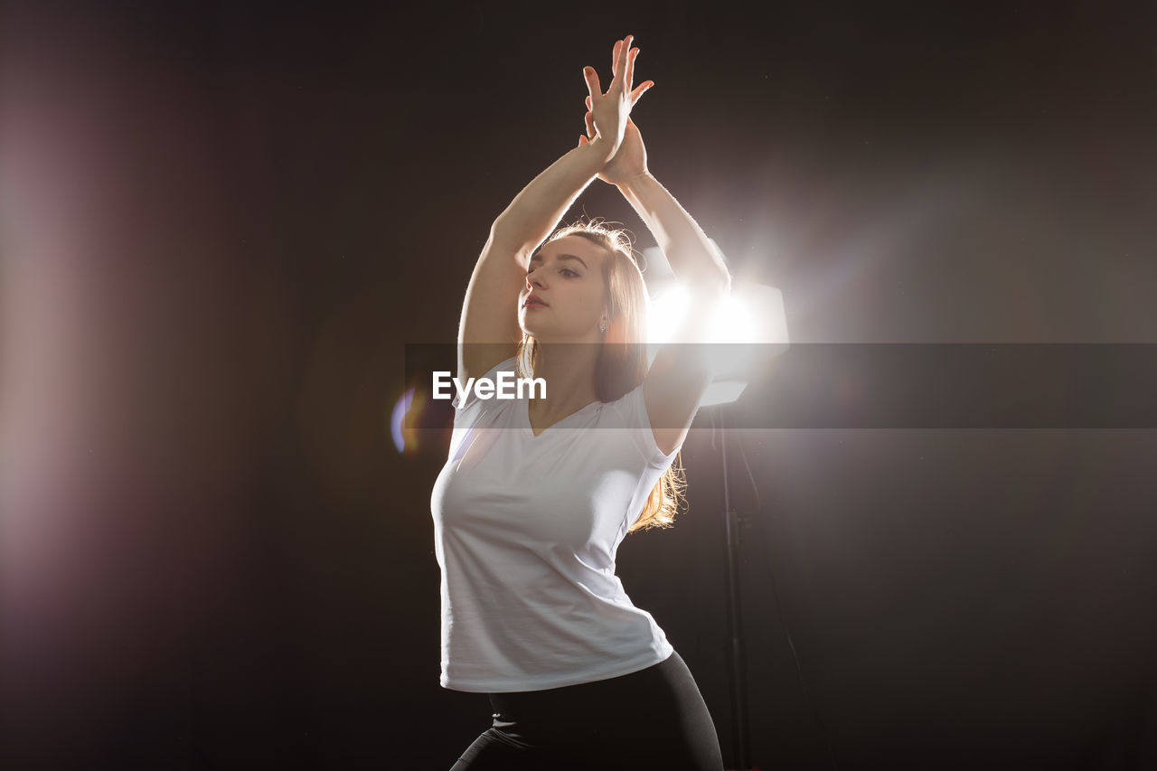 Woman standing by illuminated lighting equipment against black background