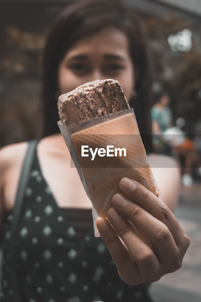 Portrait of woman showing ice cream while standing outdoors