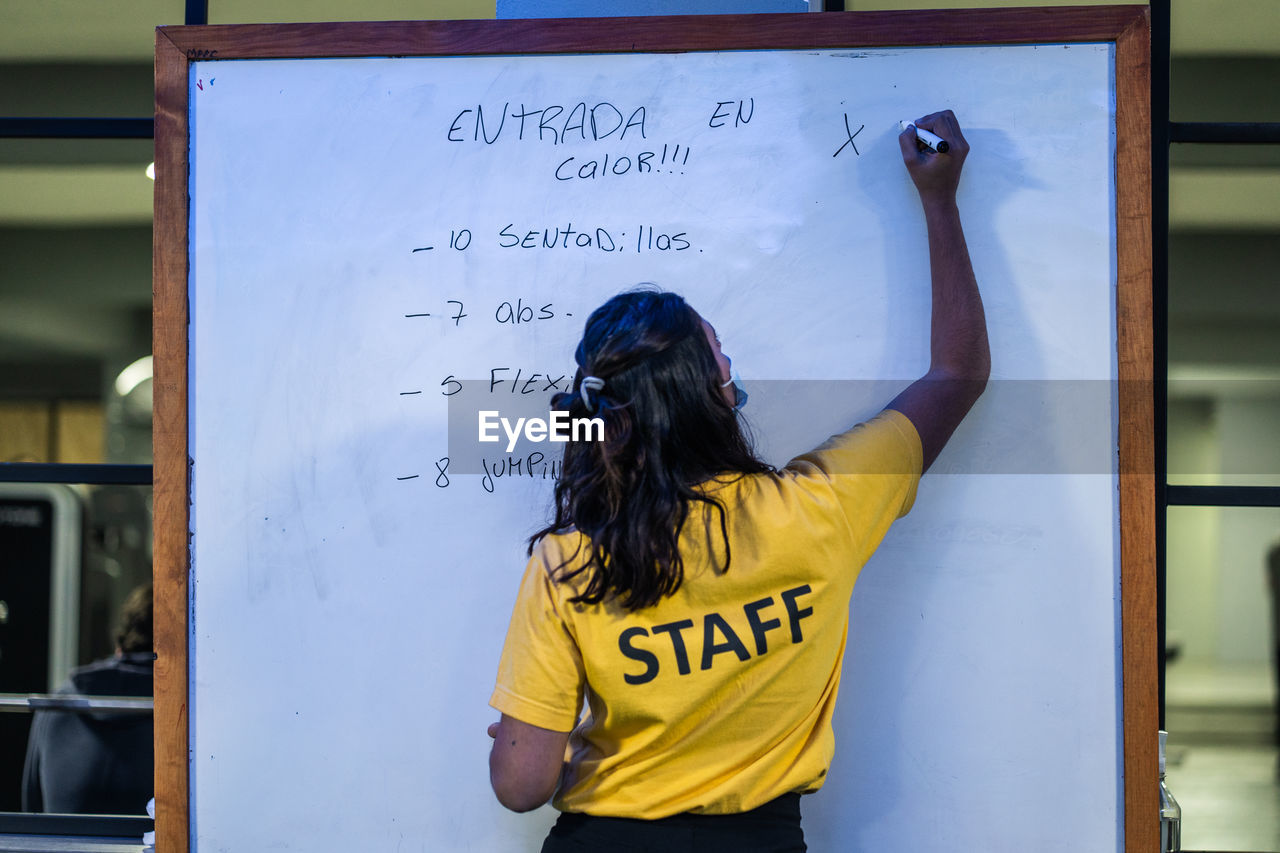 Rear view of fitness coach standing against board