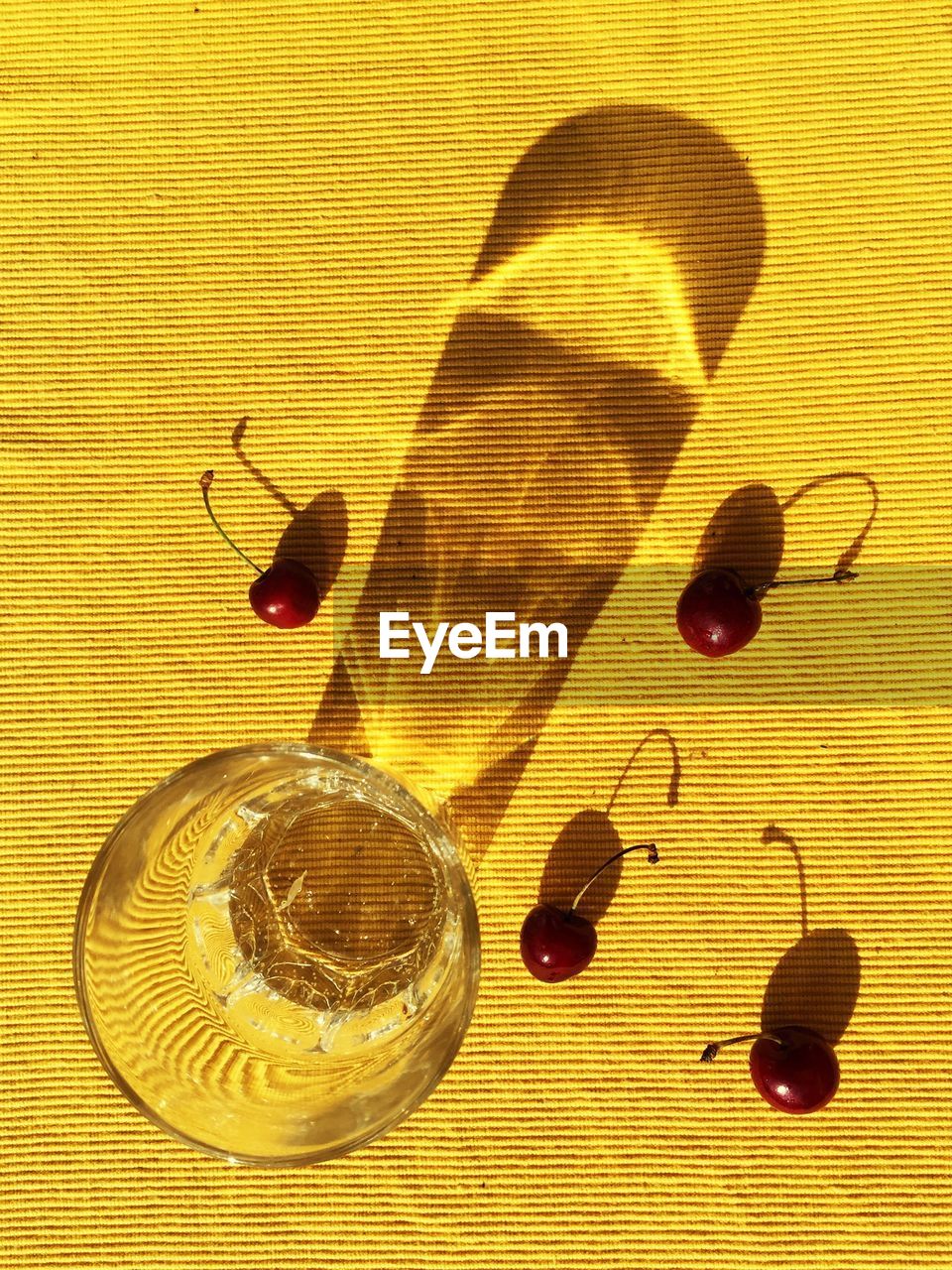 Directly above view of cherries by drinking glass on yellow textured table