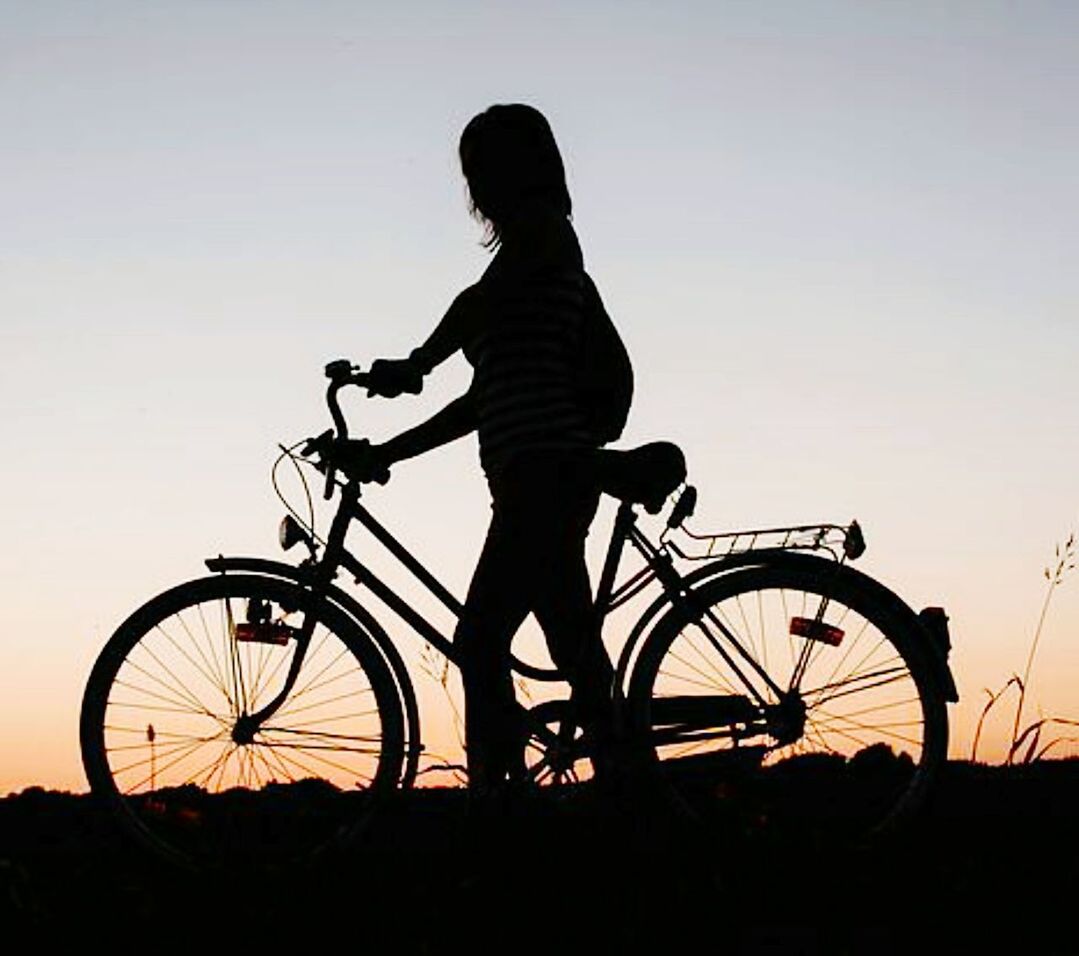 Silhouette of woman with bicycle against sky