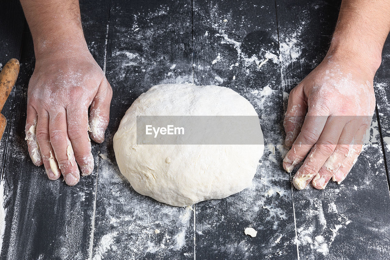 Cropped hands of person by dough on table