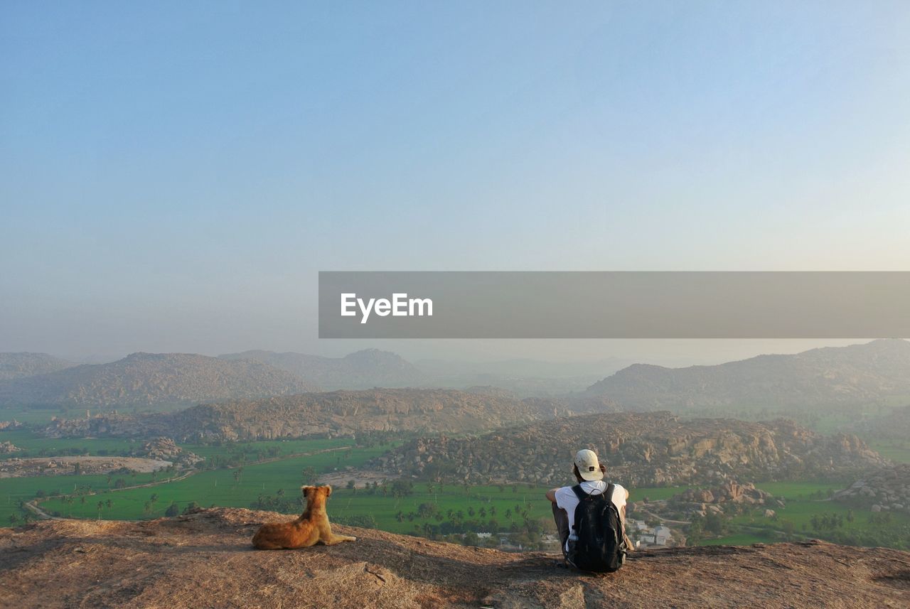 Rear view of man sitting on cliff against sky