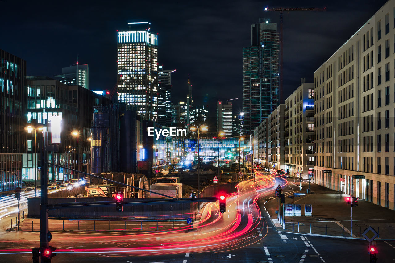 LIGHT TRAILS ON CITY STREET AMIDST BUILDINGS