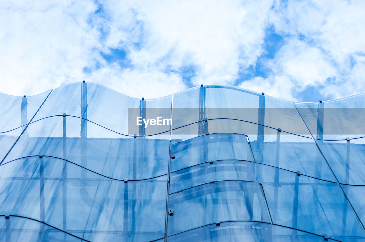 Detail of the wavy glass curtain wall facade of a nice modern building, sky and clouds reflecting